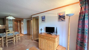 A cozy living room with a wooden cabinet, a television, and a dining area with a table and chairs.