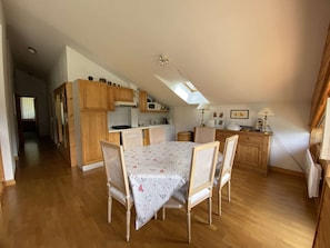 Une cuisine chaleureuse avec des meubles de rangement en bois, une table à manger avec des chaises et une lucarne.