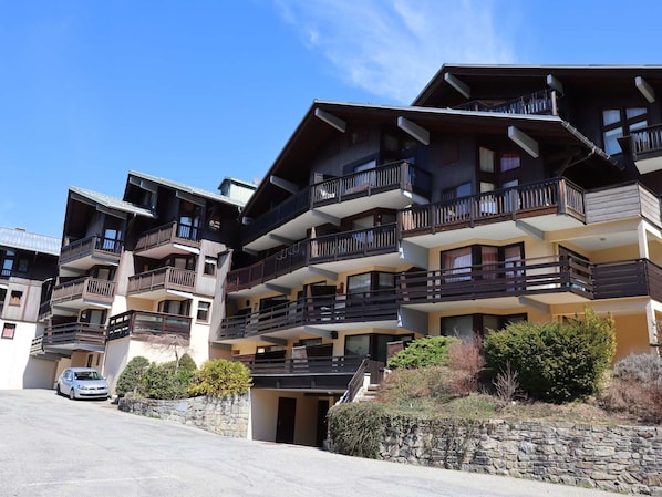 Un hôtel à plusieurs étages doté de balcons, d’un mur de soutènement en pierre et d’une voiture garée.