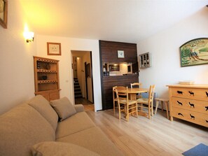 Ein gemütliches Wohnzimmer mit einer Couch, einem Holzespeise Tisch, Stühlen, einer Holzküche mit Tiermotiven und einer zum anderen Raum führenden Treppe.