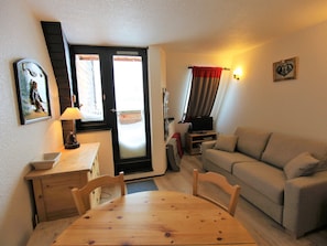 Ein gemütliches Wohnzimmer mit Holztisch, einer Couch, einem Fernseher und einer zur Außenseite führenden Tür.