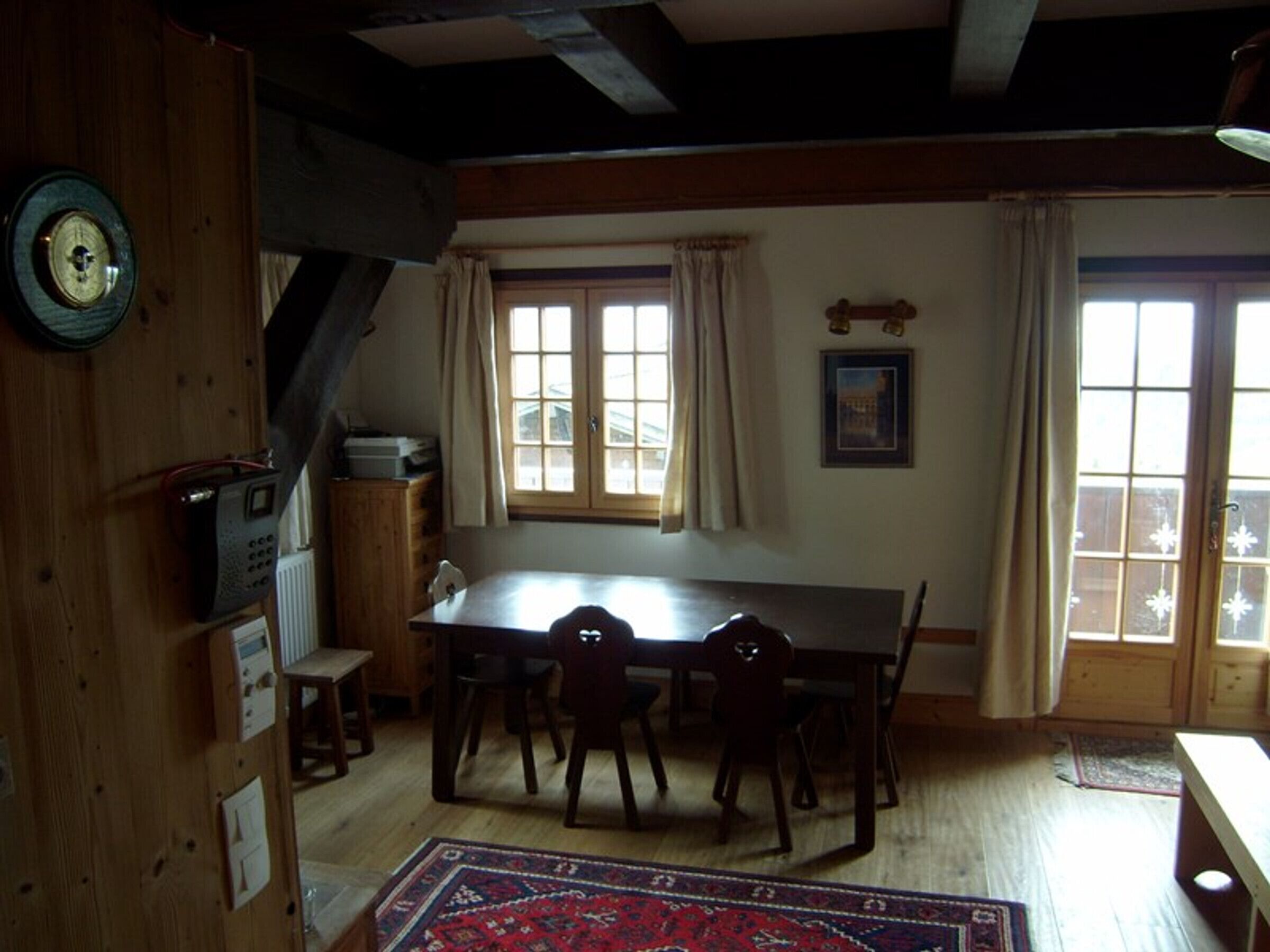 A dining room with a wooden table, chairs, a clock, and a window with curtains.