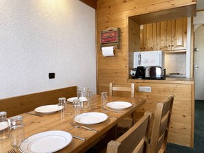 A wooden dining table set with plates, glasses, and cutlery, with a kitchen visible through an open doorway.