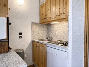 A compact kitchen with wooden cabinets, a built-in dishwasher, and a granite countertop.
