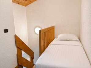 A small, single-bed room with a wooden headboard, white walls, and a round light fixture.