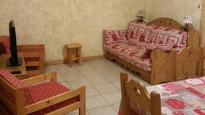 Ein gemütliches Zimmer mit einer Holzsofa, zwei Holzstühlen, einem kleinen Holztisch und einem Fernseher.