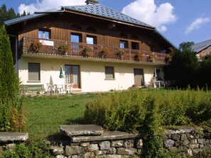A chalet with a balcony, outdoor seating, and a stone wall in front. - Cozy Studio for 4 with Mezzanine, Wi-Fi, and Parking, 400m from Chavannes Gondola (Les Gets)