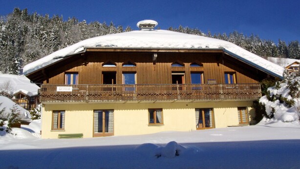 Eine Holzhütte mit Balkon, umgeben von schneebedeckten Bäumen.