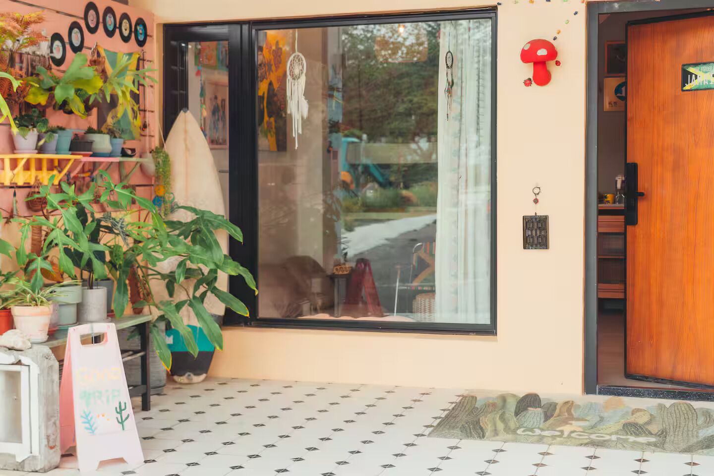 A storefront with a variety of plants, a large window, and a wooden door.