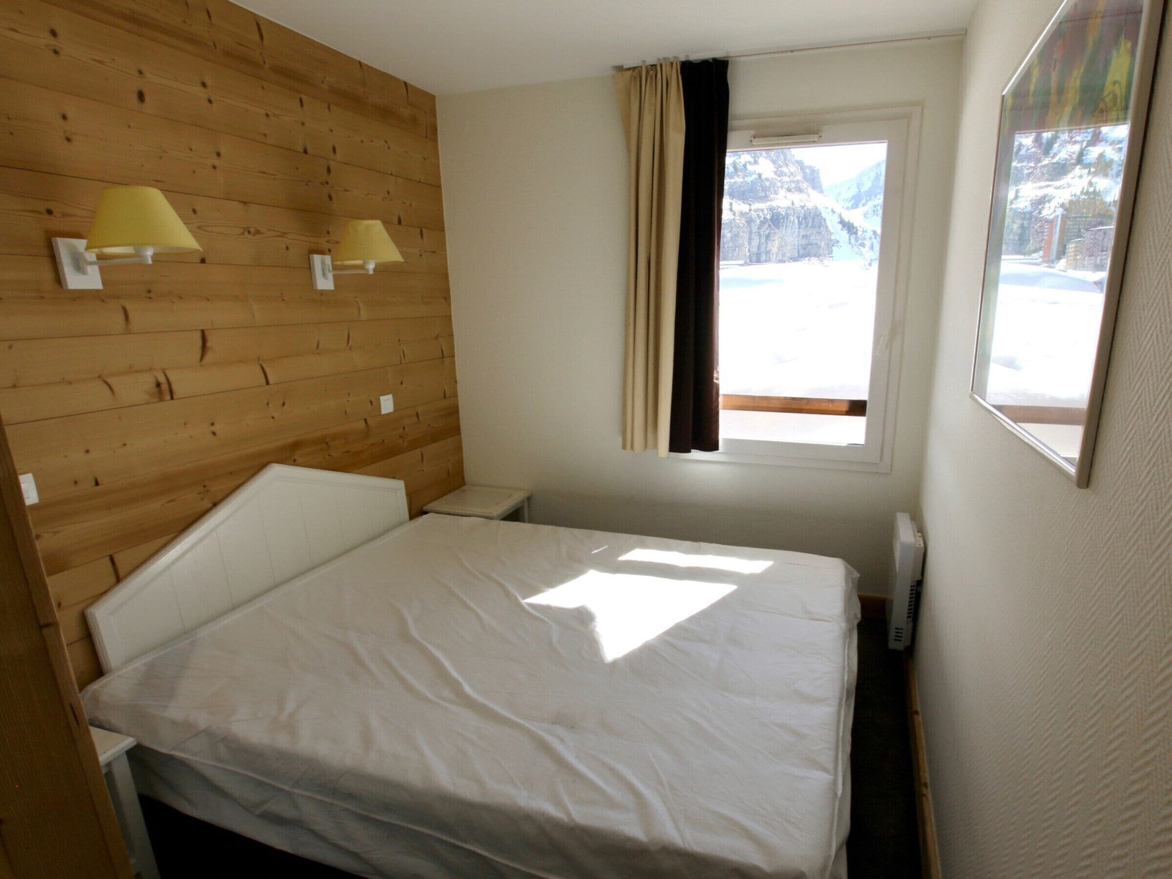A bedroom with a wooden headboard, two bedside lamps, a window with curtains, and a view of mountains.