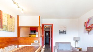 A compact living space with a wooden dining table, a grey sofa, and a small kitchenette. - Charming 2-room cabin, central, sleeps 6 (Avoriaz)