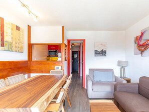 Ein gemütlicher Wohnbereich mit Holztisch, grauem Sofa und einer kleinen Küchenzeile.