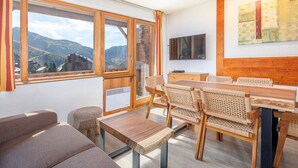 A modern room with large windows, a dining table, chairs, a sofa, and a TV. - Charming 2-room cabin, central, sleeps 6 (Avoriaz)