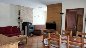 Una sala de estar acogedora con pared de ladrillo, un mueble de televisión de madera, un sofá y un comedor con sillas de madera.