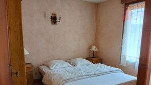 Un dormitorio con cama, mesita de noche, lámpara y ventana con cortinas.
