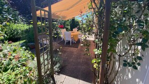 Ein überdachter Patio-Bereich mit einer Pergola, Gartenmöbeln und üppiger Bepflanzung.