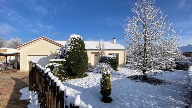 Ein Wohnhaus mit Garage, Holzzaun und schneebedeckten Bäumen.