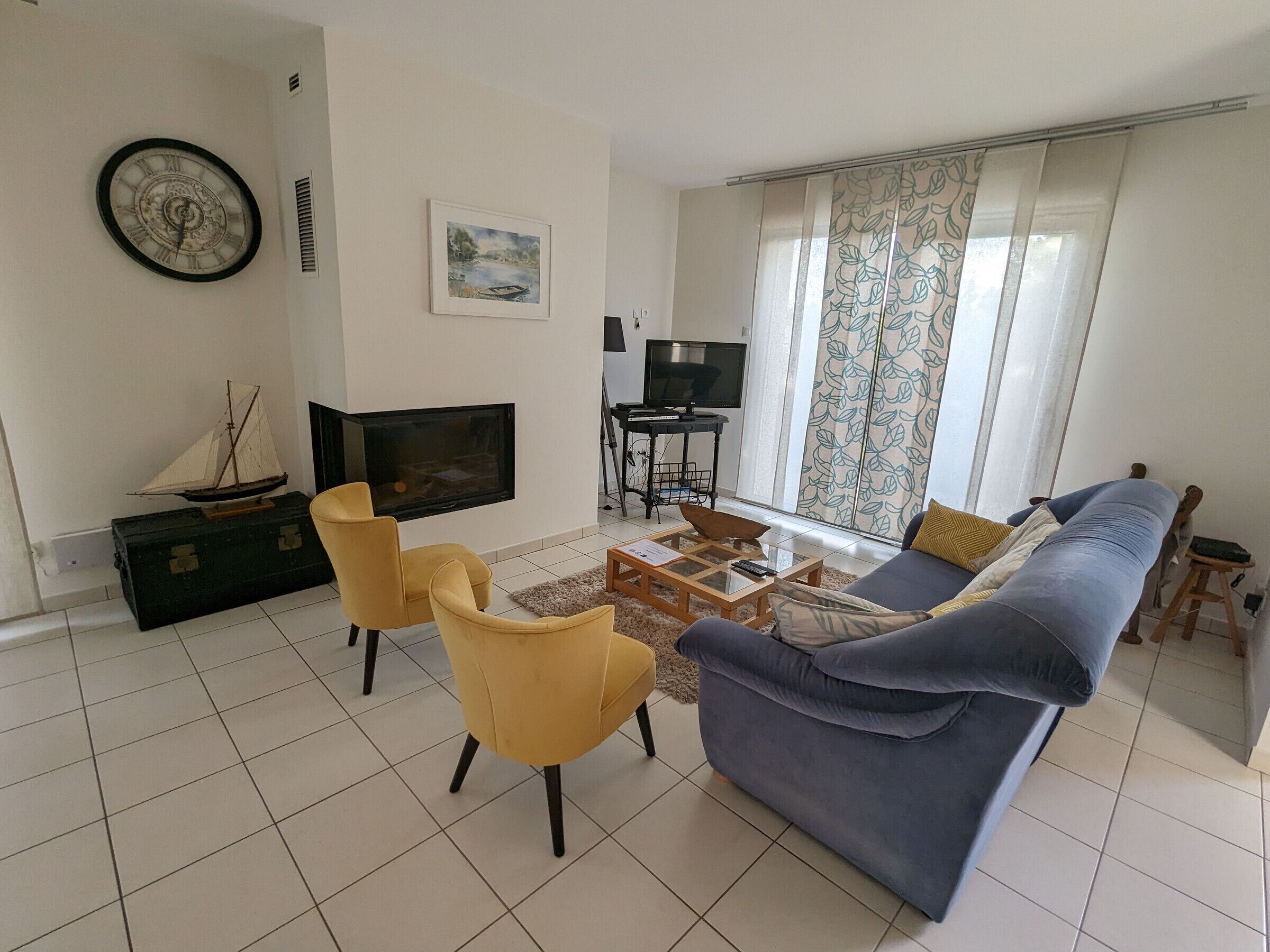 Ein Wohnzimmer mit einer Couch, zwei gelben Sesseln, einem Fernseher, einem Kamin und einem Gemälde an der Wand.
