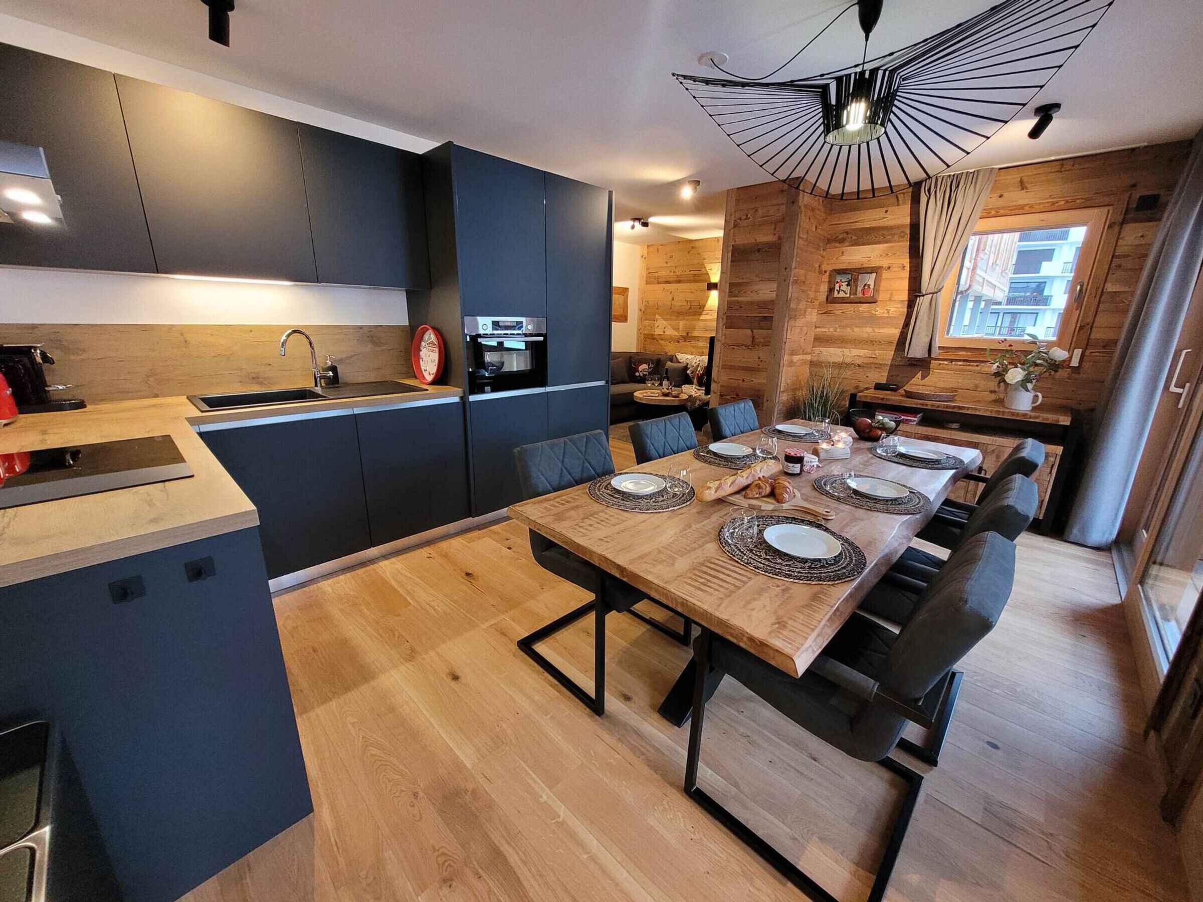 A modern kitchen with dark cabinets, a wooden dining table set for six, and a unique ceiling light fixture.
