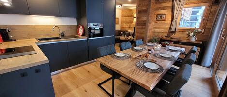 A modern kitchen with dark cabinets, a wooden dining table set for six, and a unique ceiling light fixture.