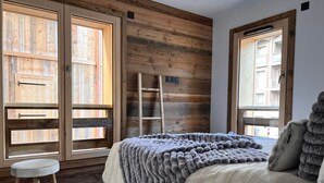 A bedroom with a wooden slat wall, a bed with a grey blanket, a ladder, and a small stool. - Cosy apartment for 6 in Les Gets with WIFI and terrace (Les Gets)