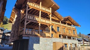 A multi-story wooden building with balconies and a stone base, likely a hotel or lodge. - Cosy apartment for 6 in Les Gets with WIFI and terrace (Les Gets)