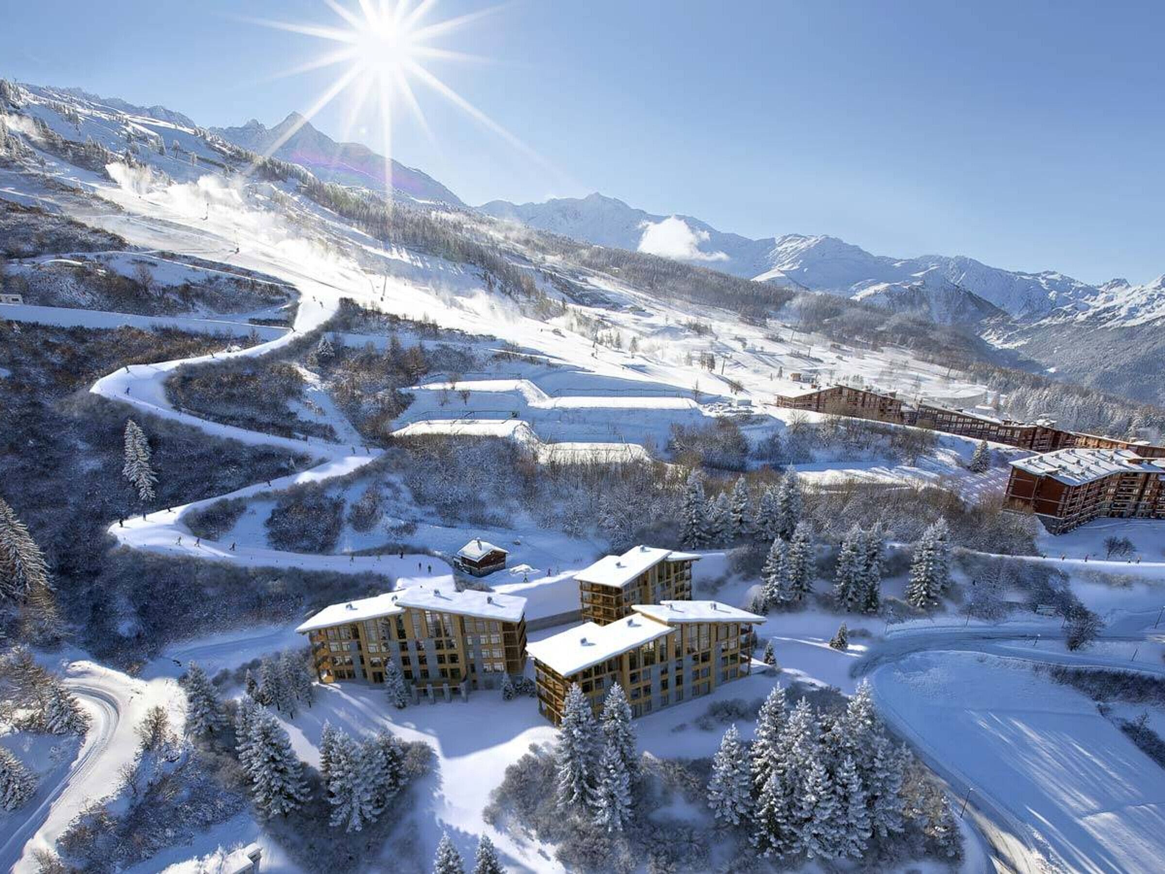 Ein verschneites Bergresort mit mehreren Gebäuden, darunter eine große Lodge und kleinere Blockhütten, umgeben von Skipisten und Bäumen.