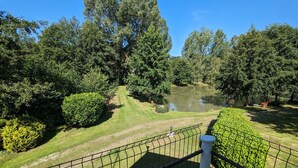 Blick auf einen Park mit einem Teich, umgeben von Bäumen und einer gepflegten Rasenfläche.