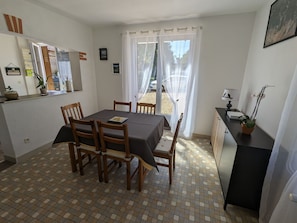 Un coin repas avec une table et des chaises, une petite cuisine avec un comptoir et des placards, et une vue sur l’extérieur par une fenêtre.