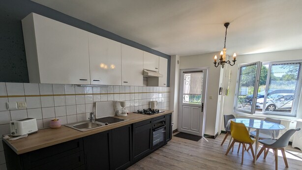 Een moderne keuken met witte kastjes, een houten aanrecht en een eethoek met een glazen tafel en stoelen.