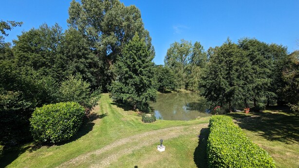 Ein gepflegter Garten mit Teich, ordentlich geschnittenen Hecken und verschiedenen Bäumen.