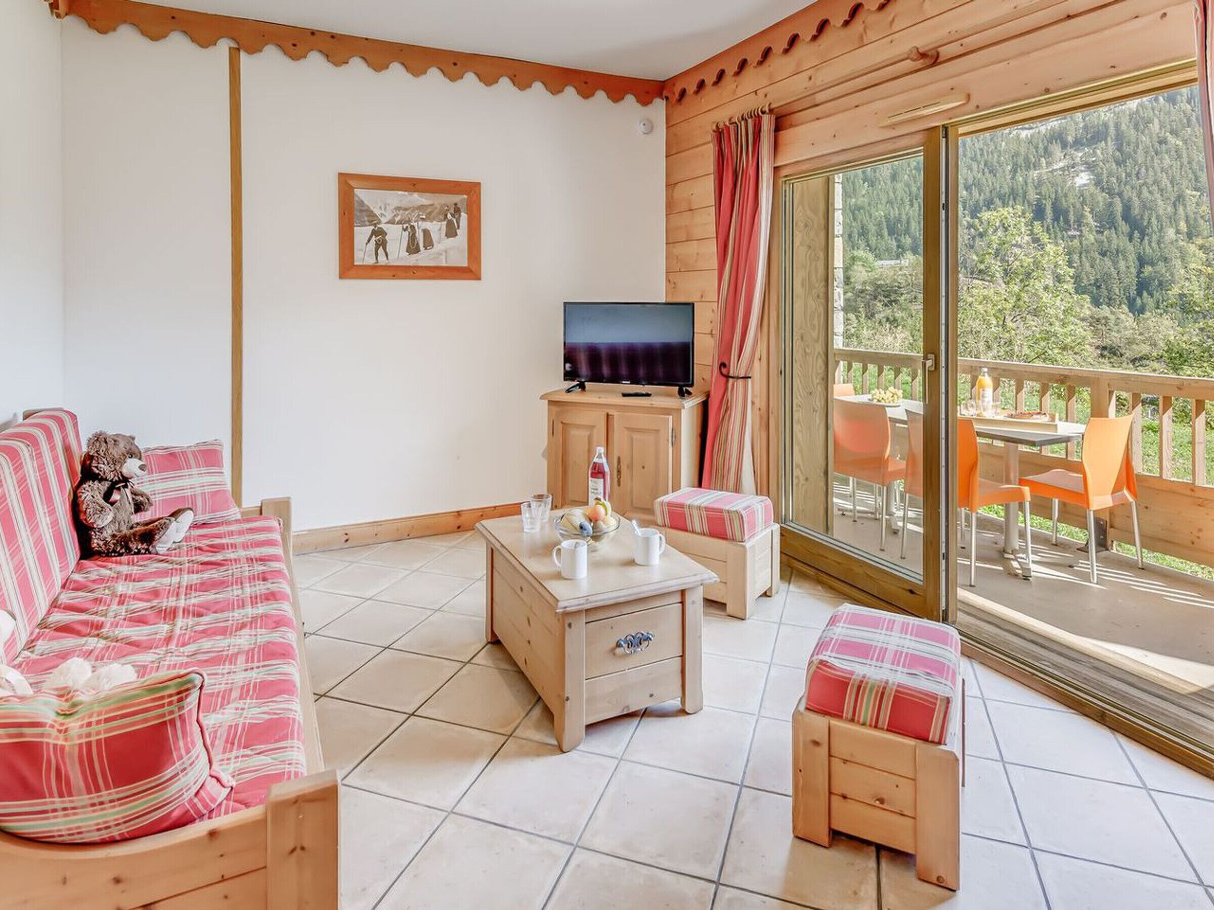 A cozy room with a sofa, a small table, a TV, and a balcony with a table and chairs.