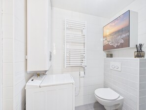 Ein modernes Badezimmer mit einer weißen Toilette, einer integrierten Waschmaschine, einem Heizkörper und einem gerahmten Bild an der Wand.