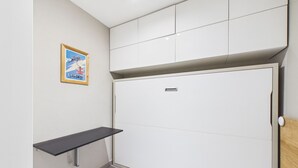 A room with a white wardrobe, a small shelf, and a framed poster on the wall.