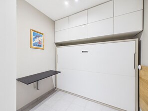 A room with a white wardrobe, a small shelf, and a framed poster on the wall.