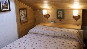 A wooden room with a bed, two wall-mounted lights, and a framed picture.