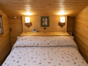 A cozy wooden room with a bed, two wall-mounted lamps, a framed picture, and a small clock.