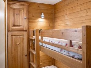 Un lit superposé en bois, doté d’une tête de lit, d’une table de chevet et d’un placard avec une poignée en forme de cœur.
