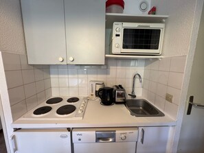 A compact kitchenette with a stove, microwave, toaster, and sink.