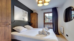 Ein Schlafzimmer mit einem Bett, einem Holzschrank, einem an der Wand hängenden Kunstwerk, einem Fenster mit Vorhängen und einem runden Spiegel.