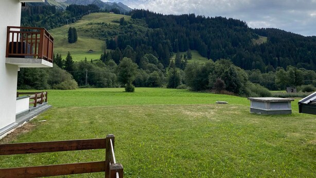 En vy över ett gräsbevuxet fält med en byggnad och berg i bakgrunden.