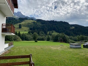 A view of a grassy field with a building and mountains in the background. - Charming 2-room with west terrace, near slopes, includes parking (La Chapelle-d'Abondance)