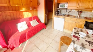 Ein gemütliches Zimmer mit einer roten Couch, Holzschränken, einer Mikrowelle, einer Kaffeemaschine und einem kleinen Tisch mit Schüsseln.