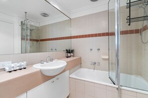 Ein modernes Badezimmer mit einer Glastrennwand zur Dusche, einem weißen Waschbecken und einer beigen Arbeitsplatte.