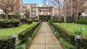 A pathway leading to a building with a covered entrance, surrounded by well-maintained hedges and trees. - Prahran 3 Bed Escape - Prime Location (Prahran)