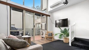 A modern living room with a sofa, a small table, a chair, and a TV mounted on the wall. - Prahran 3 Bed Escape - Prime Location (Prahran)