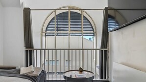 A hotel room with a bed, a round table with a book and a plant, a window with blinds, and a view of the outside. - Prahran 3 Bed Escape - Prime Location (Prahran)