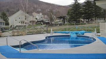 A swimming pool with a blue water slide, surrounded by a fence, with houses and a mountain in the background.