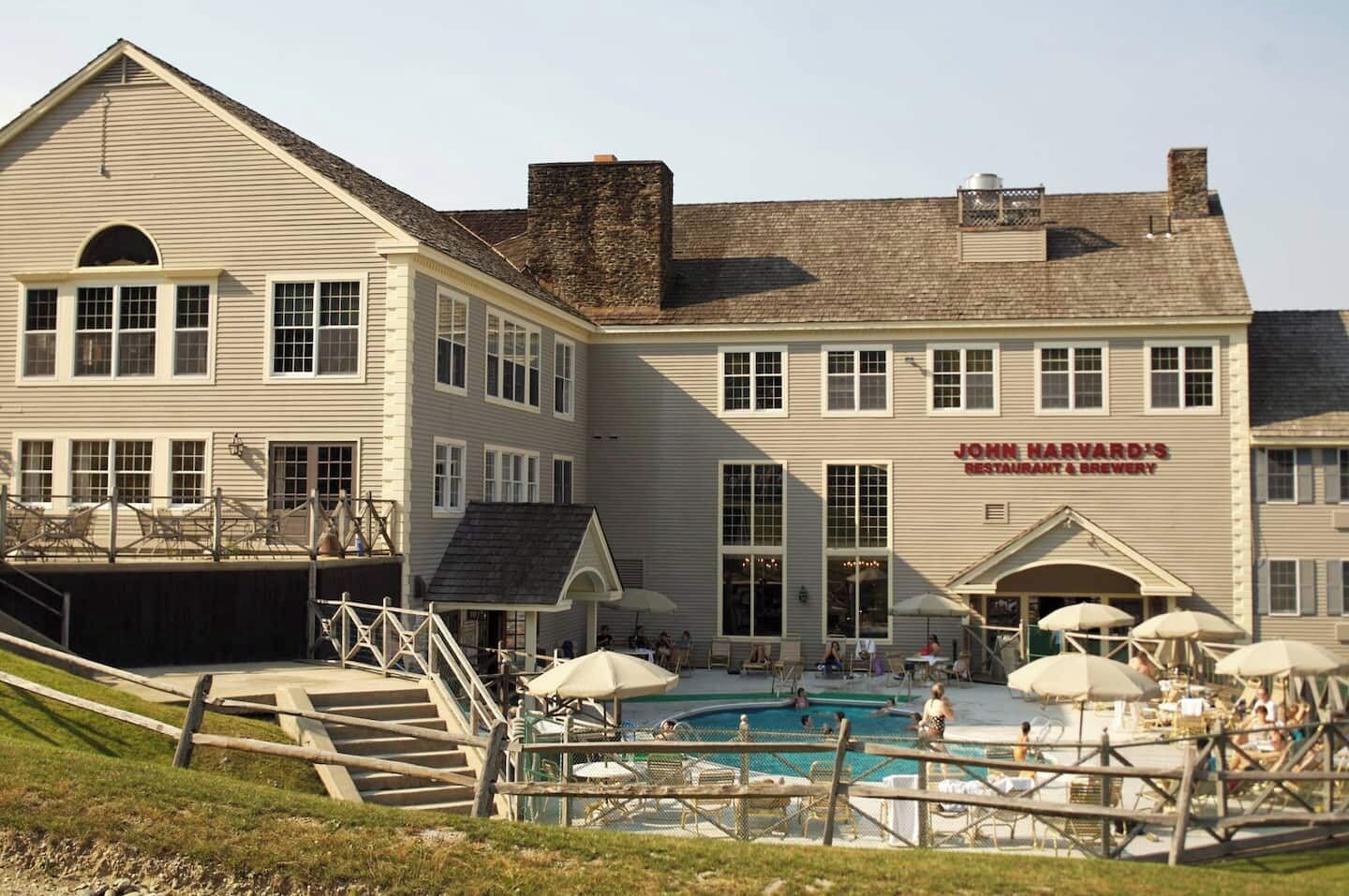 A building with a pool area, outdoor seating, and a sign for 'John Harvard's Restaurant & Brewery'.