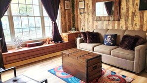 Una sala acogedora con un sofá, un cofre de madera y una alfombra estampada.